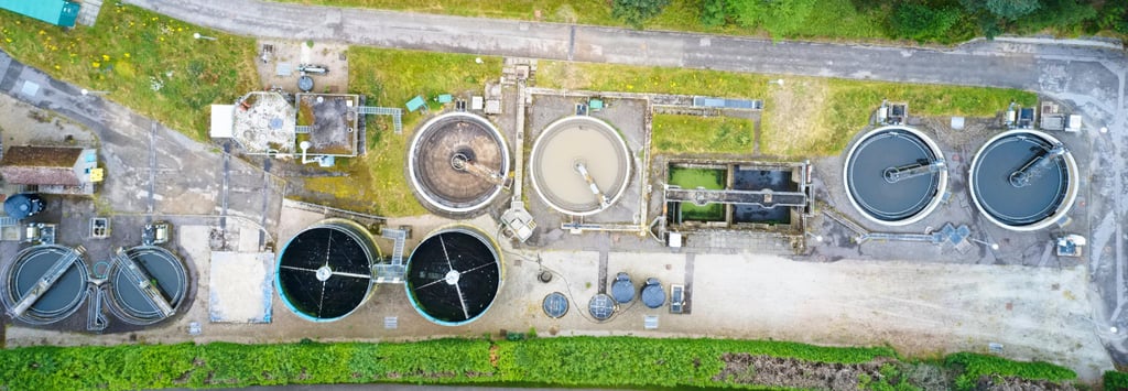 Aerial view of a wastewater treatment plant with circular tanks, green surroundings, and infrastructure.