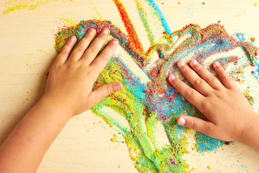 A child paints on a table with colored sand. Picture by valeriya/Adobe Stock