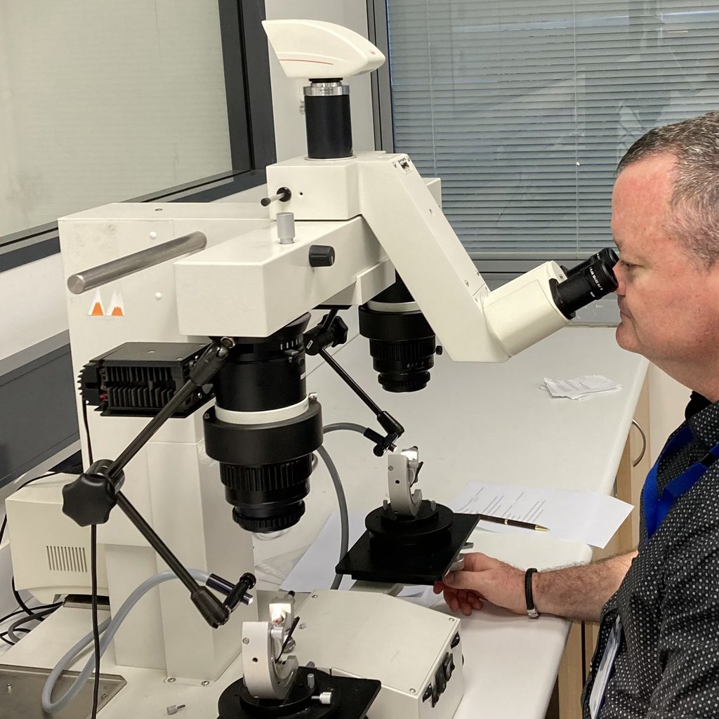 Masters by Research graduate Matthew Bolton looks at a microscope in a lab setting