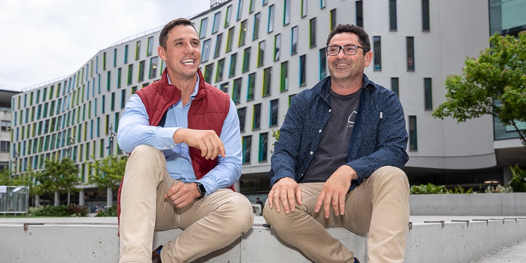 Two men seated on a ledge at UTS alumni green, engaged in conversation and enjoying the view.