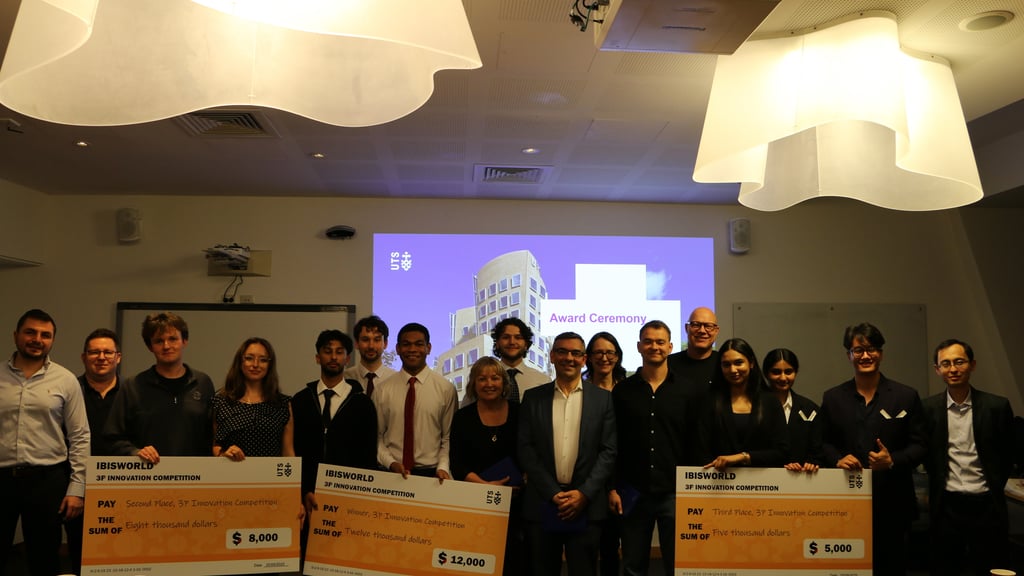 A group of students stand in a line smiling to camera while holding their oversized prize checks with the dollar amounts noted on each, 1st prize is $12,000 second prize is $8,000 and third prize $5,000.