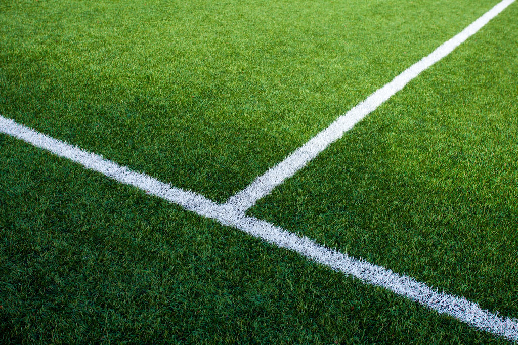Close-up of a sports field showing bright green artificial turf with two white boundary lines intersecting at a corner marking.