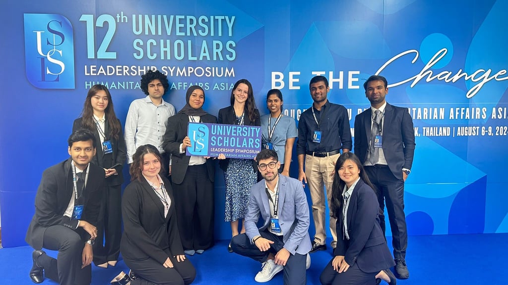 Sai at the 12th University Scholar Leaders Symposium in Bangkok. A group of attendees stand in front of the Symposium sign.