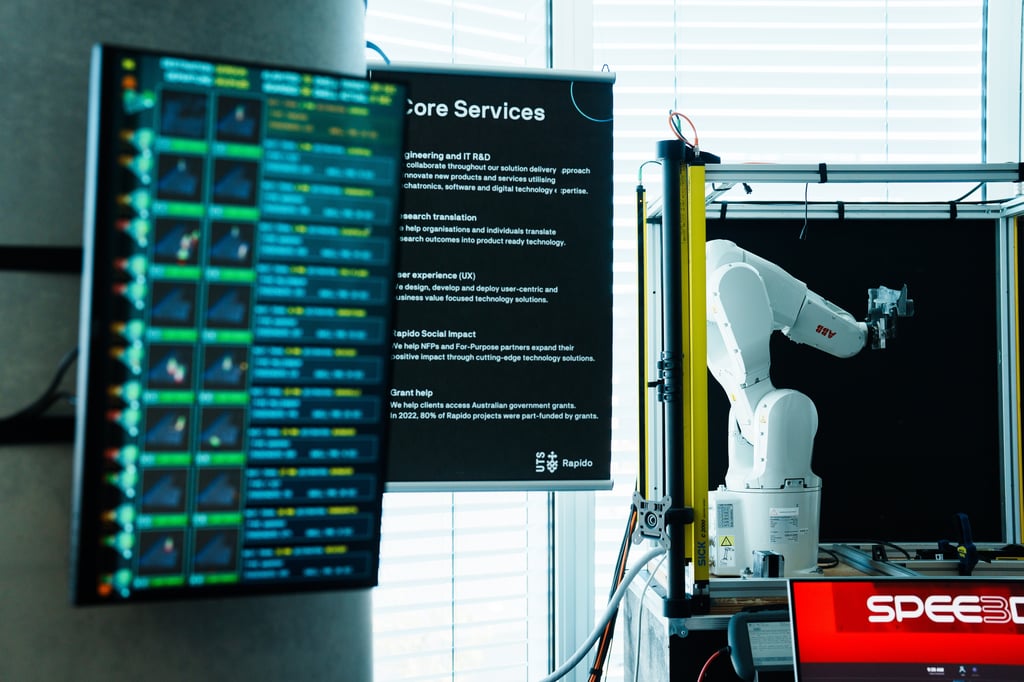 Large screen showing blurred software data with a 3D printing robot alongside it