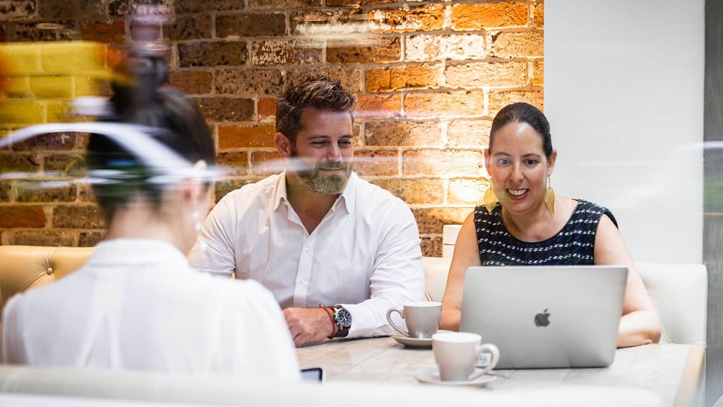 Three people sitting at a table behind glass, working on a laptop