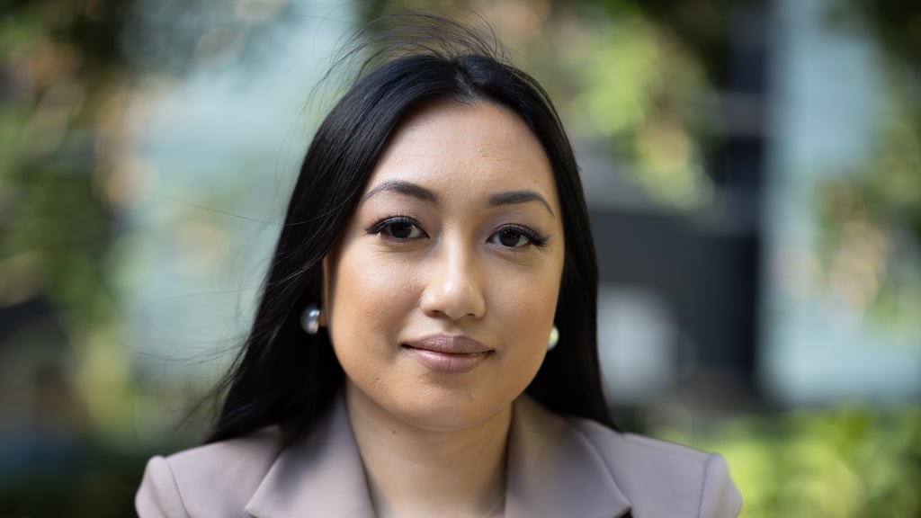 Arhita del Fierro is wearing a light brown blazer. Trees can be seen in the background.