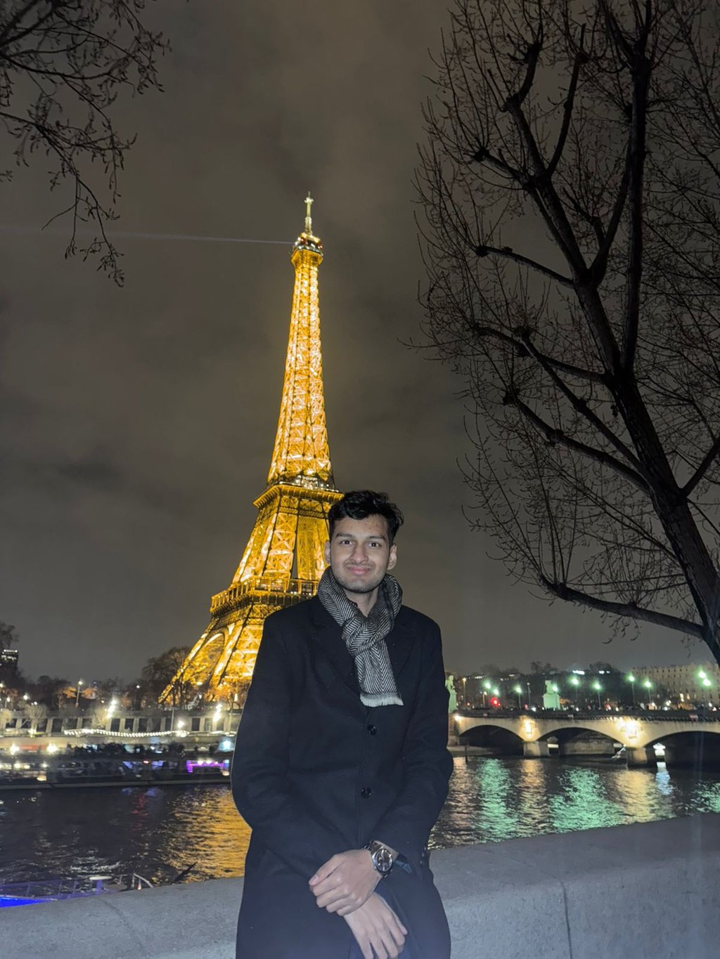 Sai in front of the Eiffel Tower in Paris at night. The tower is lit up.