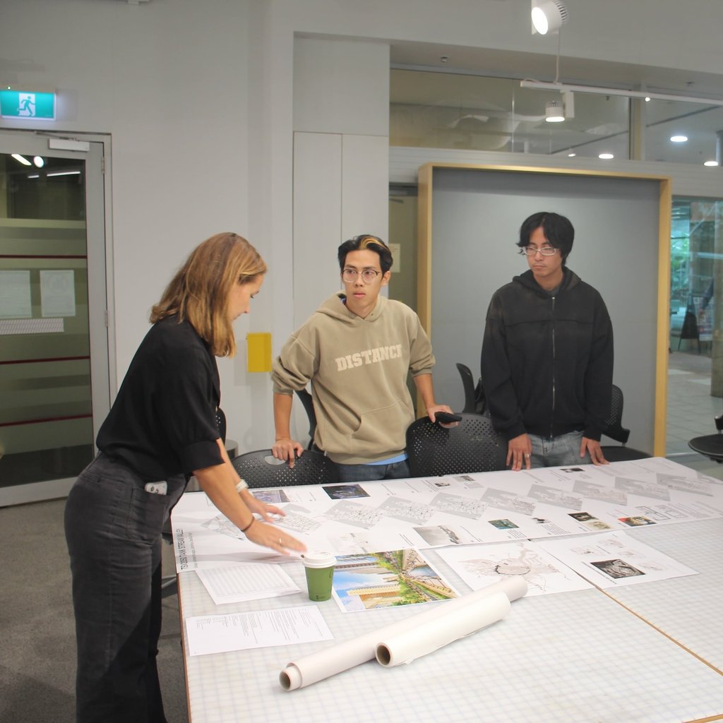 Three people looking over designs from architecture and landscape architecture students for the Tank Stream Valley