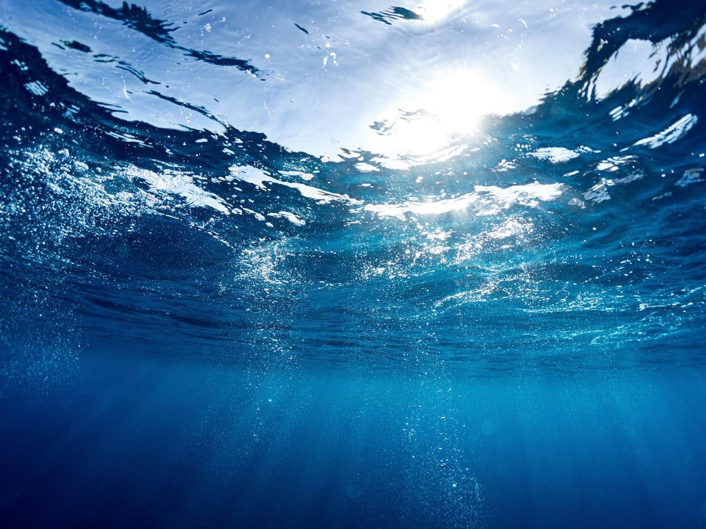Underwater view of sunlight filtering through clear blue ocean, creating shimmering patterns and a serene, peaceful atmosphere.
