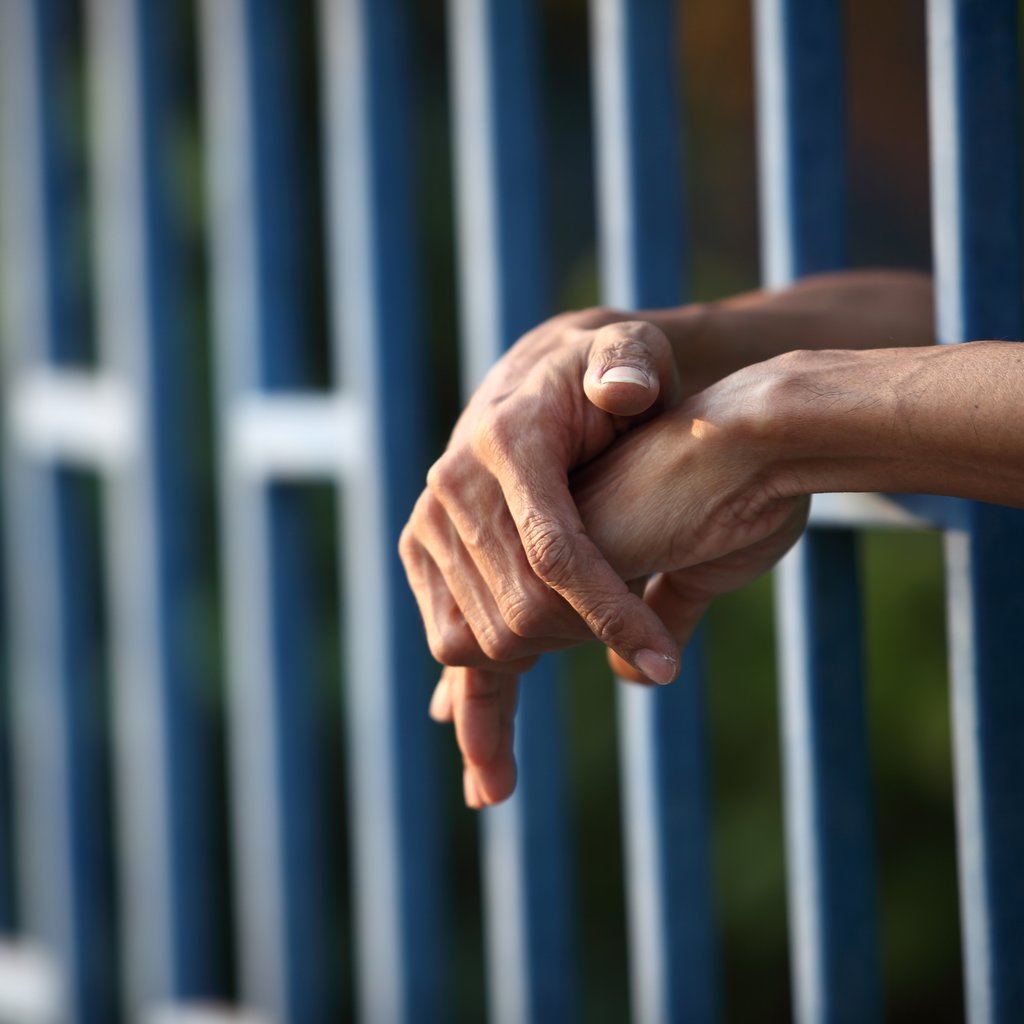 Hands through the bars of a fence