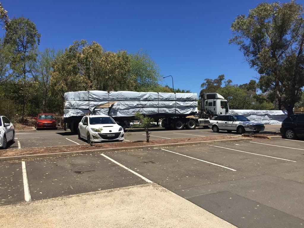 Prefabricated timber structures stacked on a flatbed track that is stopped in a parking lot.