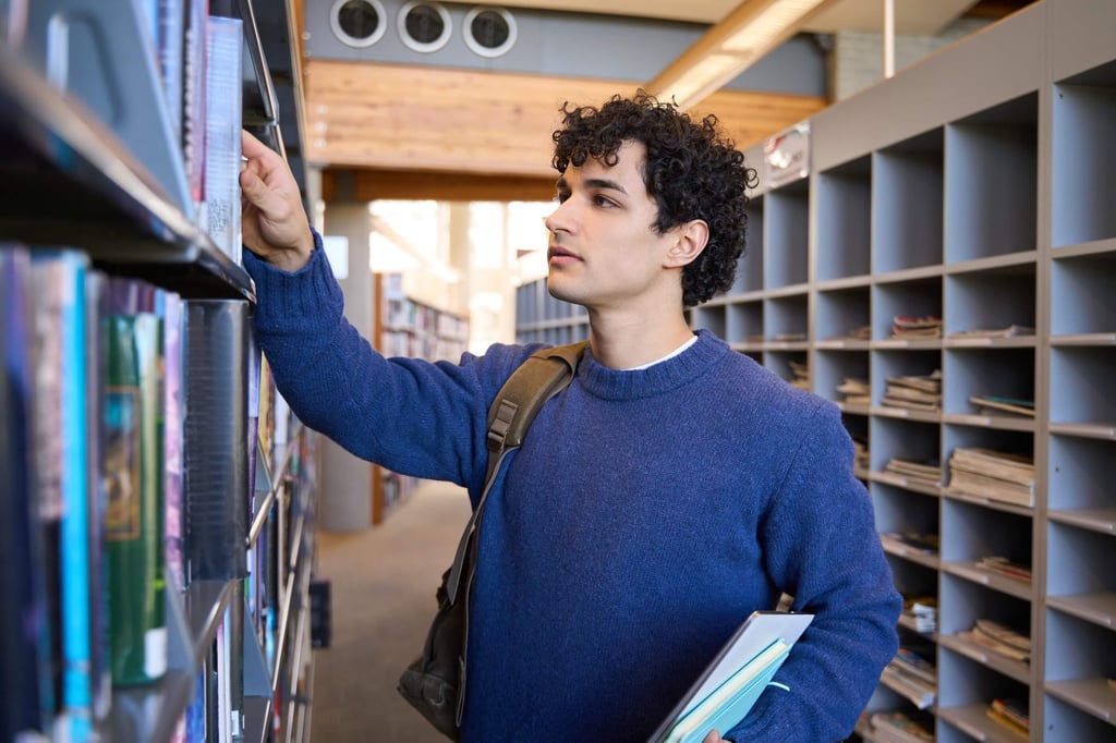 University student reaching for books on a library shelf.