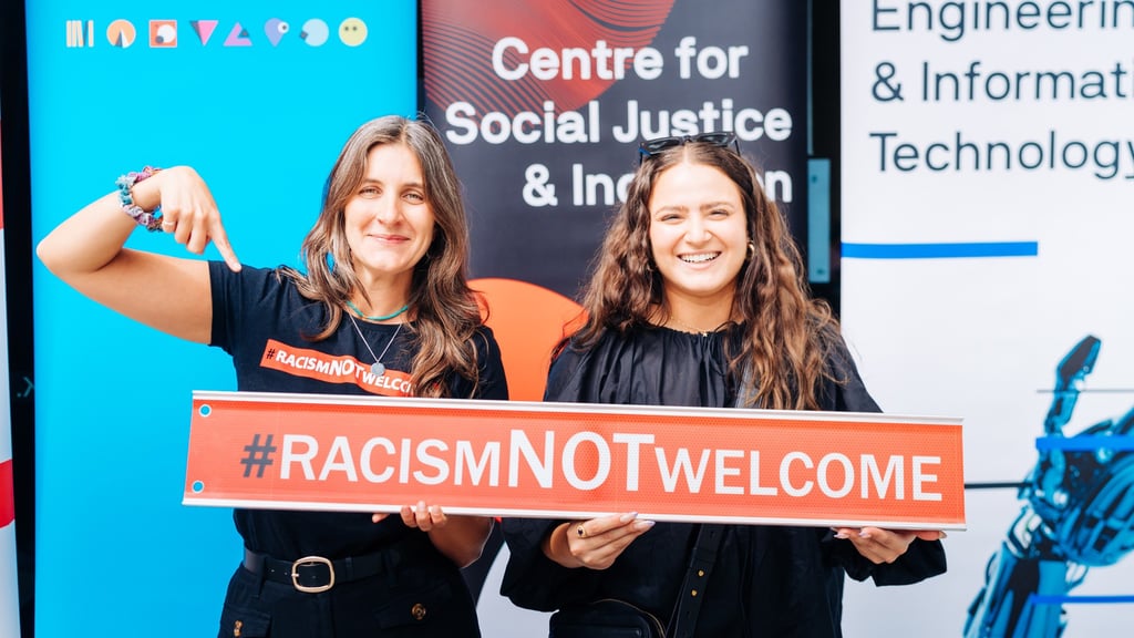 Two University of Technology Sydney staff members holding a 'Racism NOT Welcome' sign
