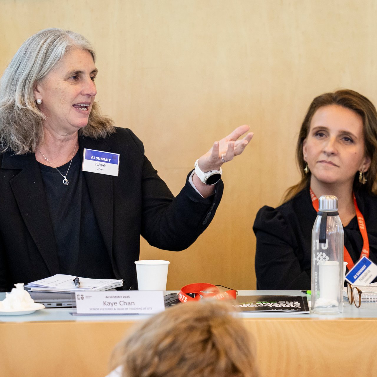 Dr. Kaye Chan addresses an audience offscreen in the UTS Business School oval classroom. She is dressed in black shirt and blazer. Behind her in the background is seated Professor Natalina Zlatevska who is watching her present.