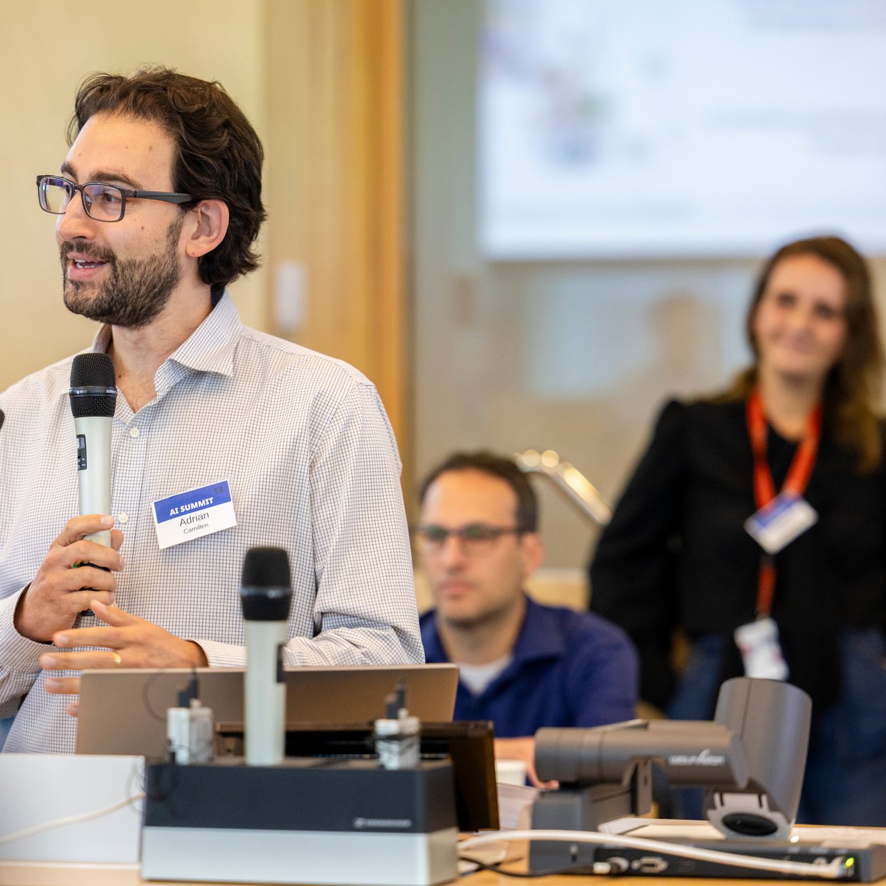 Dr Adrian Camilleri is stood before a podium in the UTS Business School Oval classroom gesturing to an audience offscreen. He is dressed in a white business shirt and several attendees are visible seated behind in the background listening in.