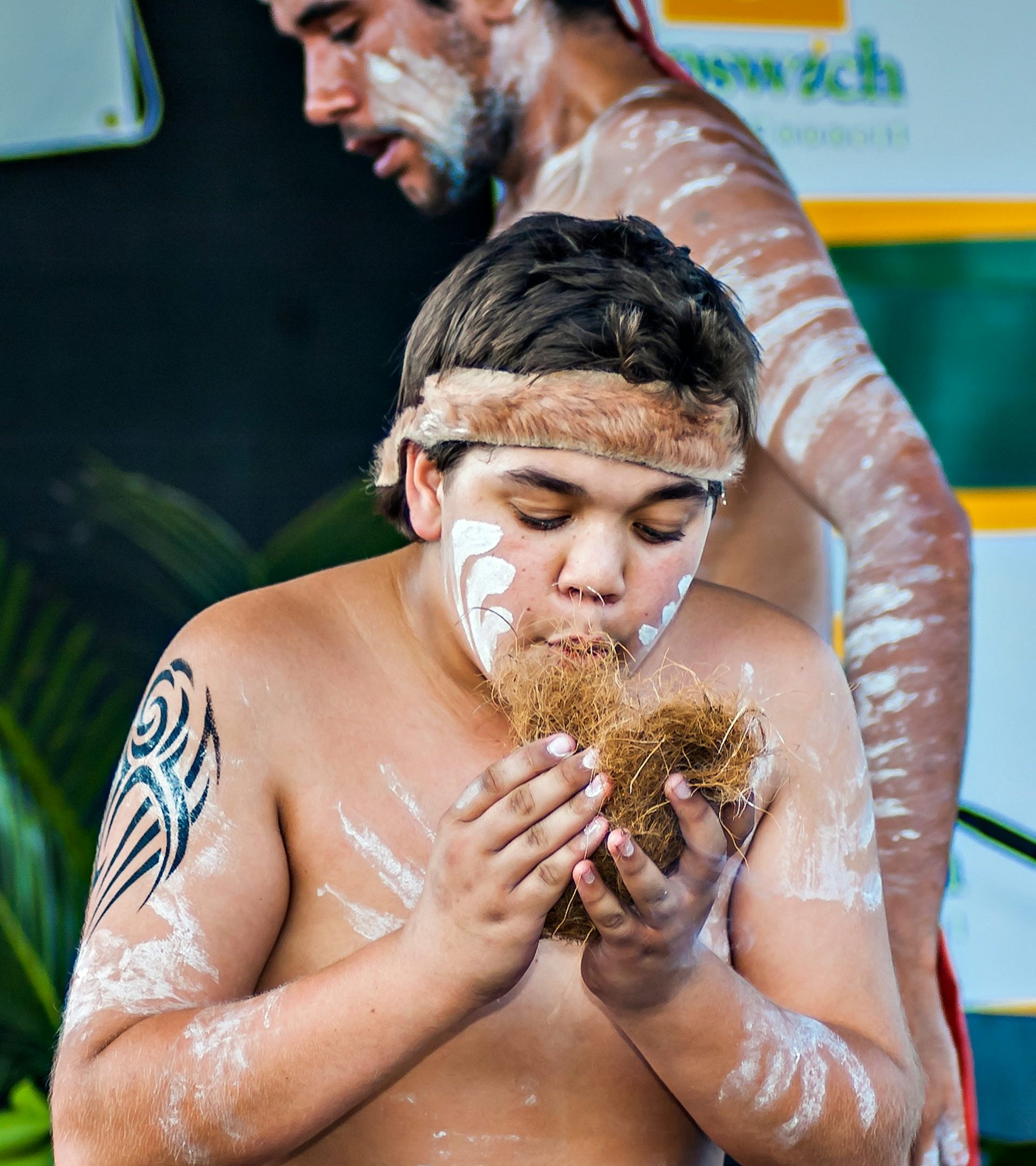 A young First Nations person stands in cultural paint, trying to ignite fire.