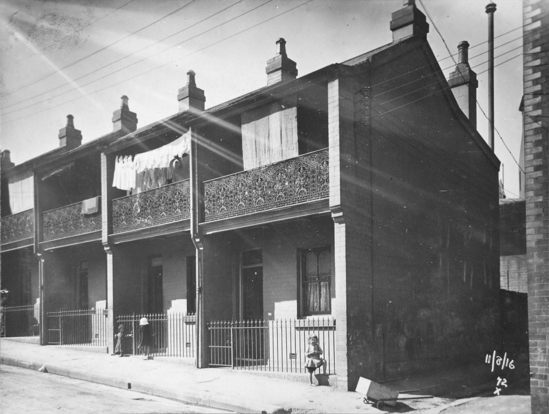 Two storey terraces with cast iron on balconies with children in front playing with a go kart. Washing / laundry on balcony.