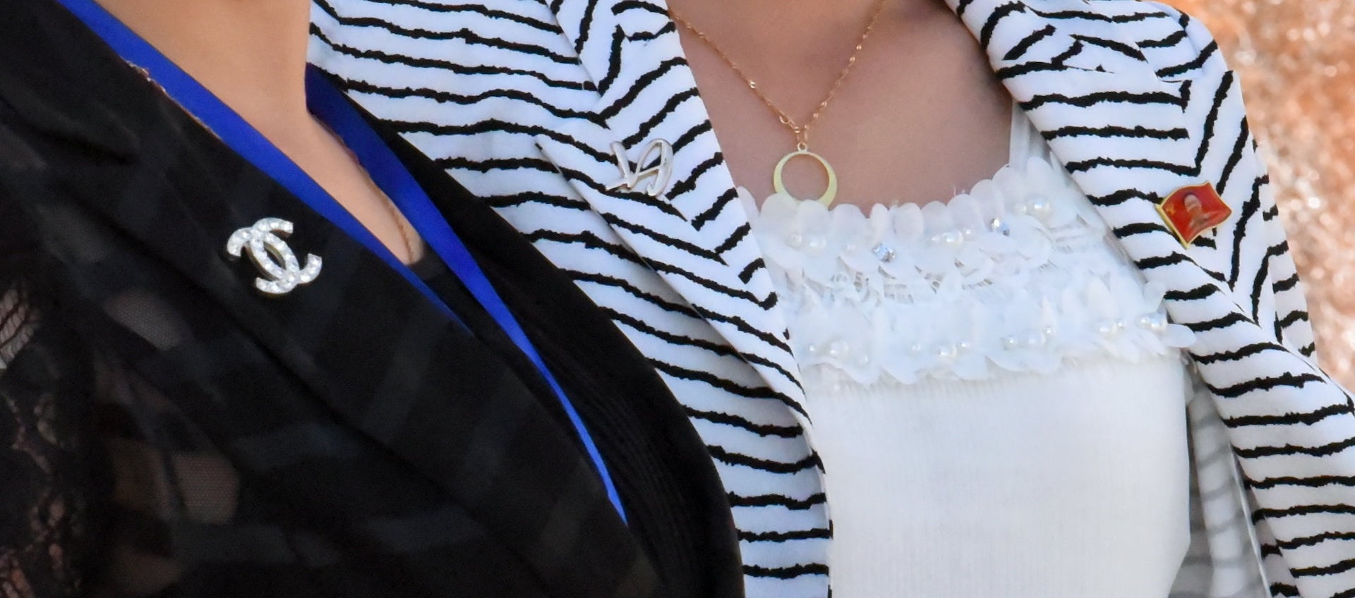Two women one with a Chanel-style brooch and another with a North Korean label pin.