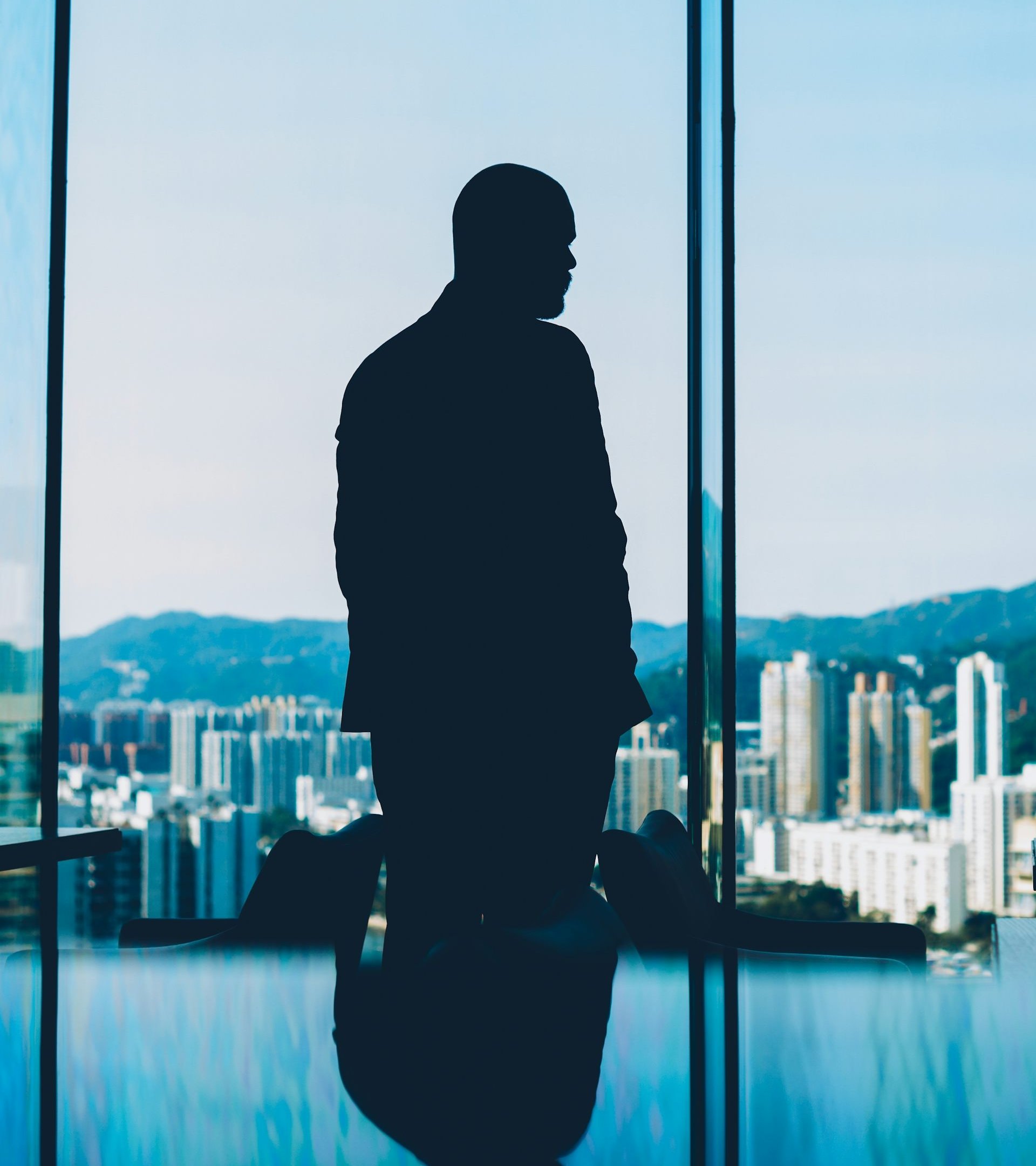 Silhouette of man looking out window at city skyline
