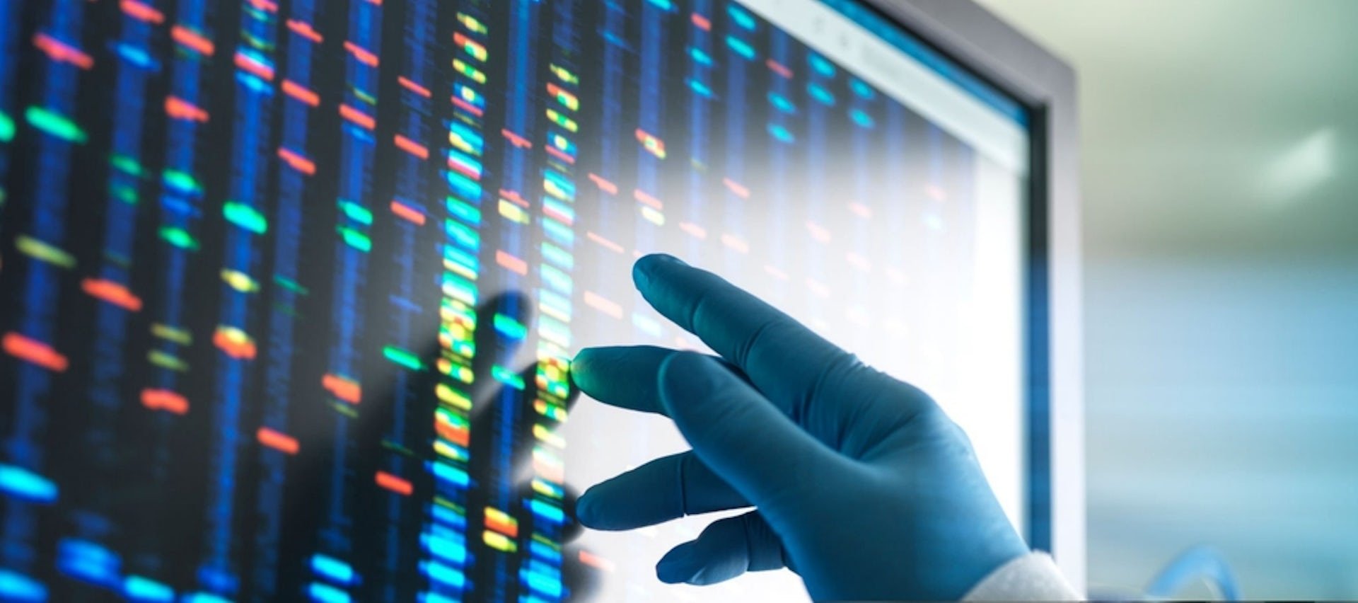 Gloved handed researcher touching screen of DNA sequences in bright colours