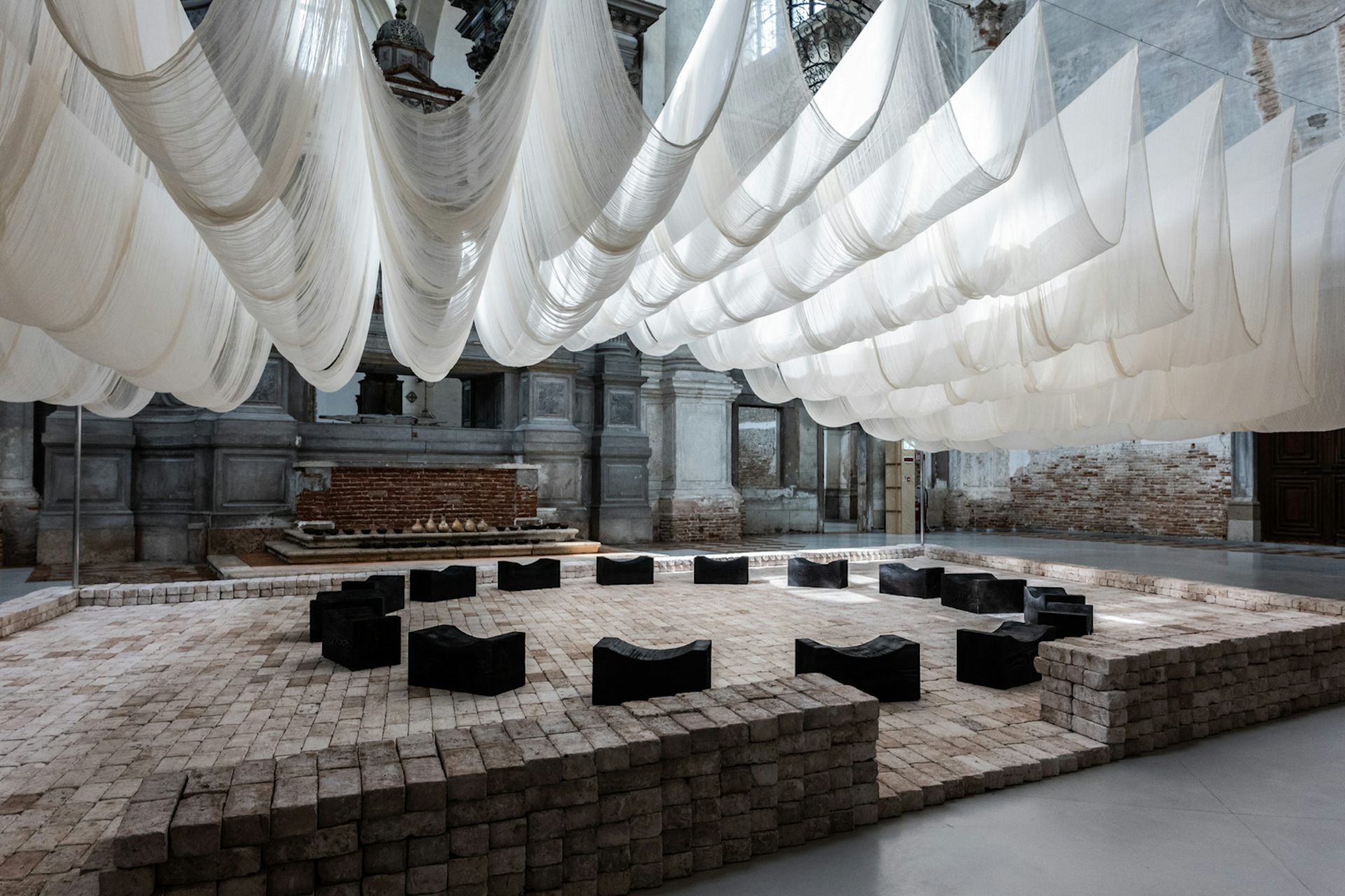White sheets billow as a roof above a circle of black benches.