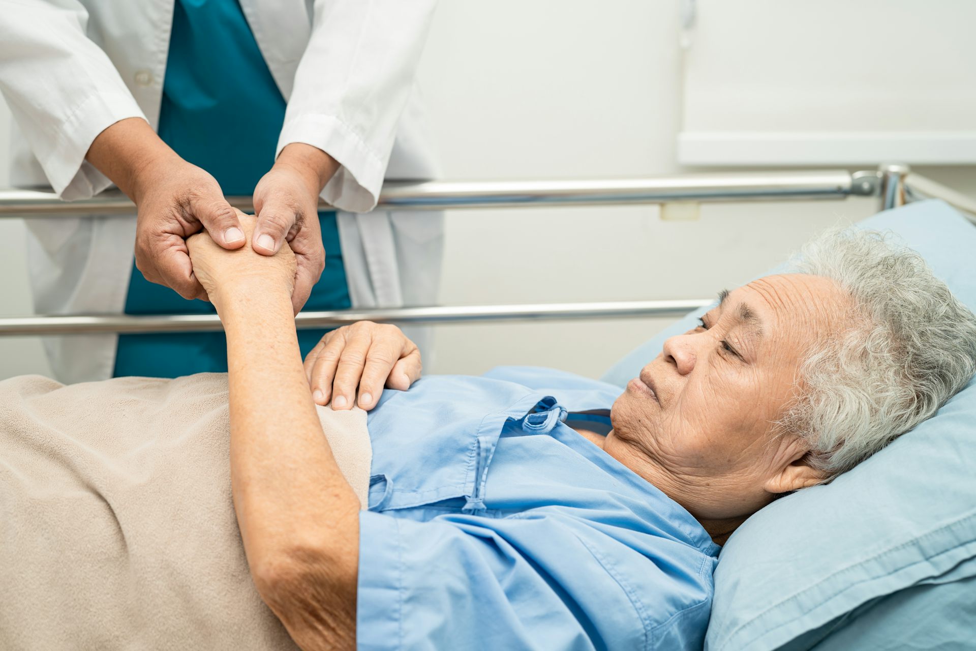 Doctor holds hands of an elderly woman in a hospital bed.