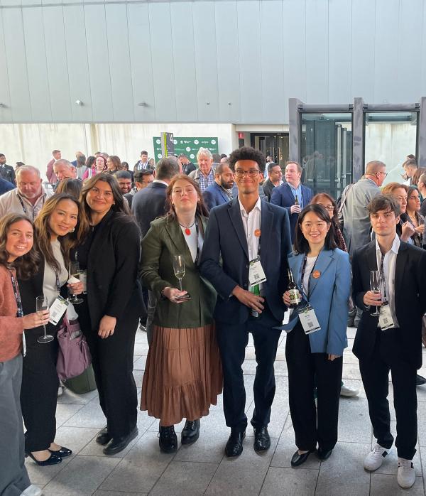 Students stand with champagne and smile at the camera
