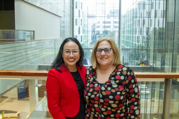 Two women stand on one of the air bridges in Building 10, smiling at the camera with arms around each other