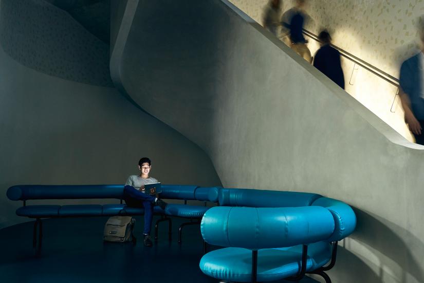 Student working on his laptop as he relaxes on a blue sofa