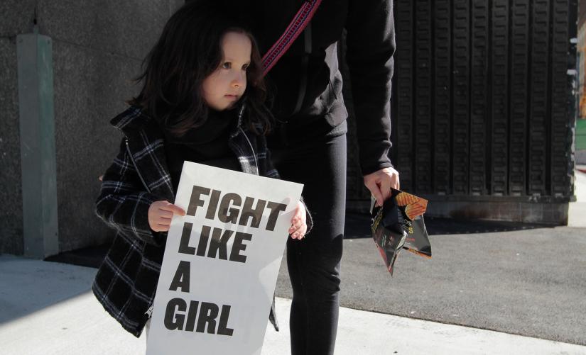 A young girl holds a sign that reads 'fight like a girl'