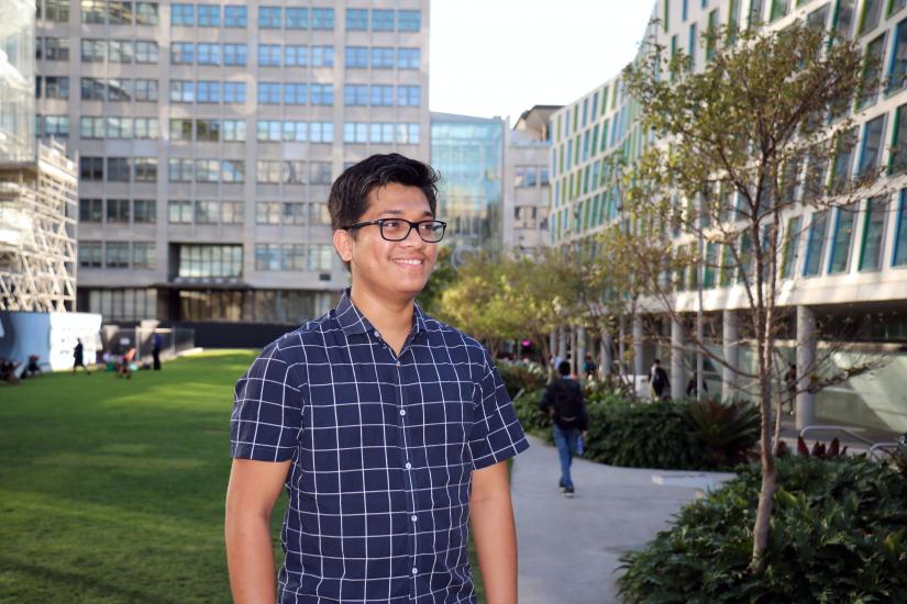 Mujibur smiling while looking off camera. UTS Alumni Green is in the background.