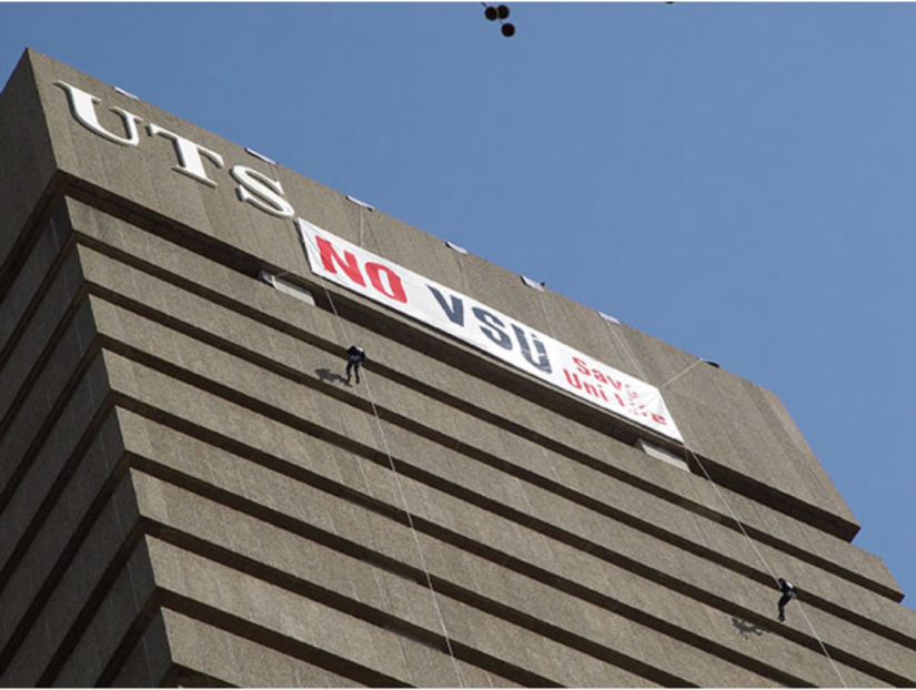Looking up at the UTS Tower with a person coming down the side. Flag on side of tower that reads 