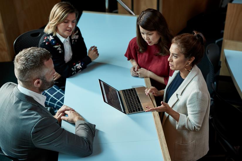 A women with laptop in discussion with one male and two female colleagues around a work table.