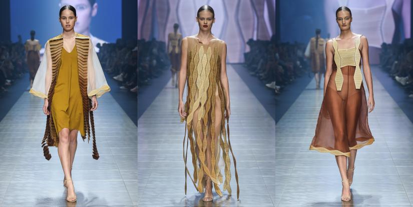 Three images side-by-side of a brightly-lit fashion runway, with a seated crowd on either side. In each image, a model wears one of Jessica’s designs. The cuts in the wood allow the pieces to flow as the models walk.