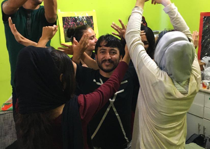 Participants in the improv. workshop at Cisarua Refugee Learning Centre circle a man raising their arms an gesturing