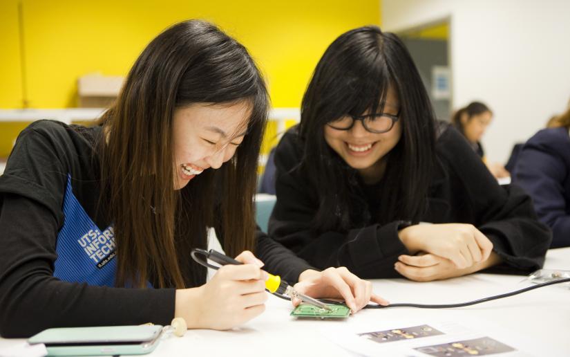 Two female engineering students sit at a desk laughing.