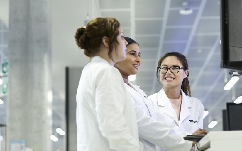 Three women in lab coats looking at computer screen.