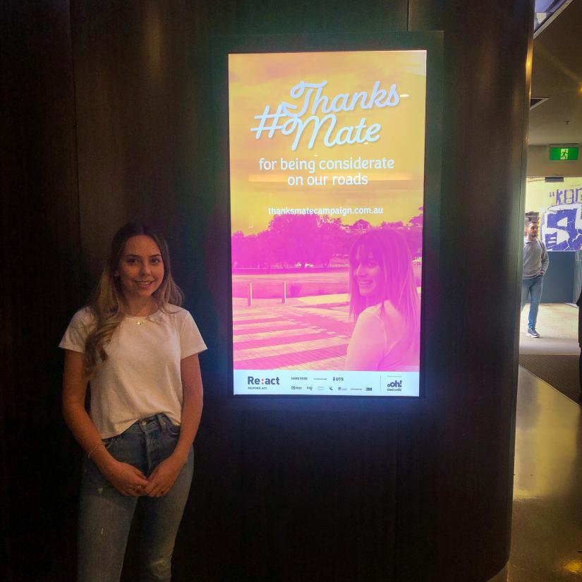 Beth Sacco stands in front of a screen displaying her thanksmate campaign