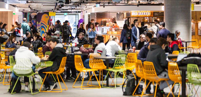 A crowded food court with colourful chairs and neon-lit takeaway counters