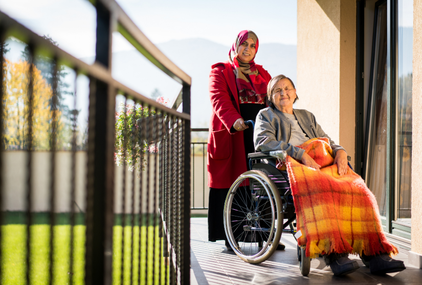 Muslim woman standing behind elderly women in wheelchair