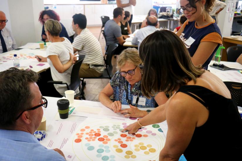 Room full of people working around tables with coloured diagrams