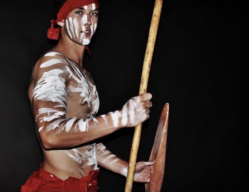 UTS Elite Athlete and First Nations person Jordan Williams wearing traditional Indigenous garments, body paint and carrying a spear and shield