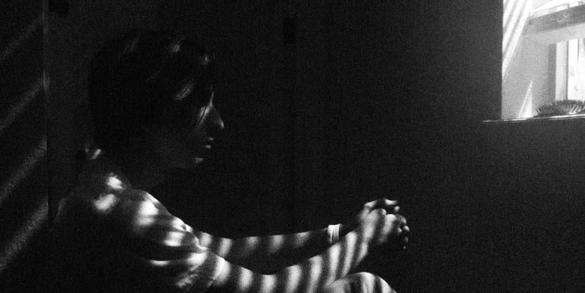 Person looking sad with shadow of window and blinds across them.