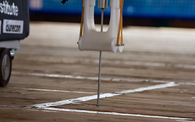 A robot arm screws a screw into a wooden floor.