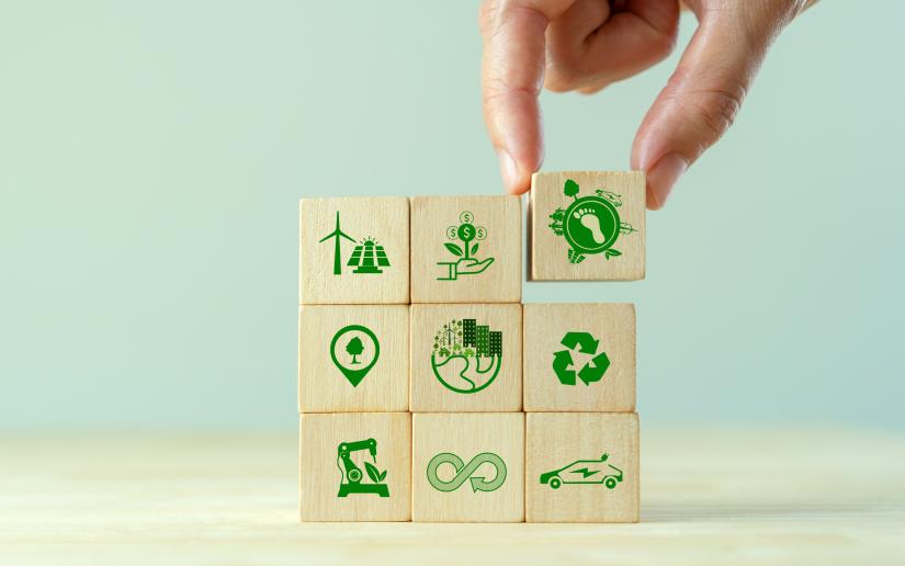 Stock picture of a hand placing wooden blocks in a square formation, each depicting a symbol of sustainable industry.
