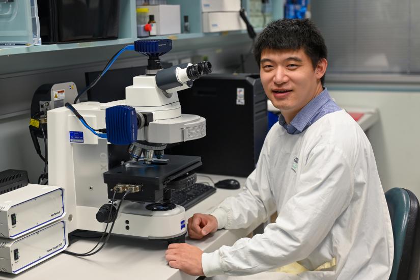 Dr Gang Liu seated in front of a microscope