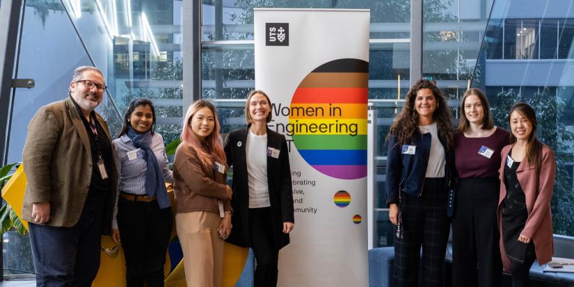 Women around the banner of Women in Engineering and IT posing in front of the banner