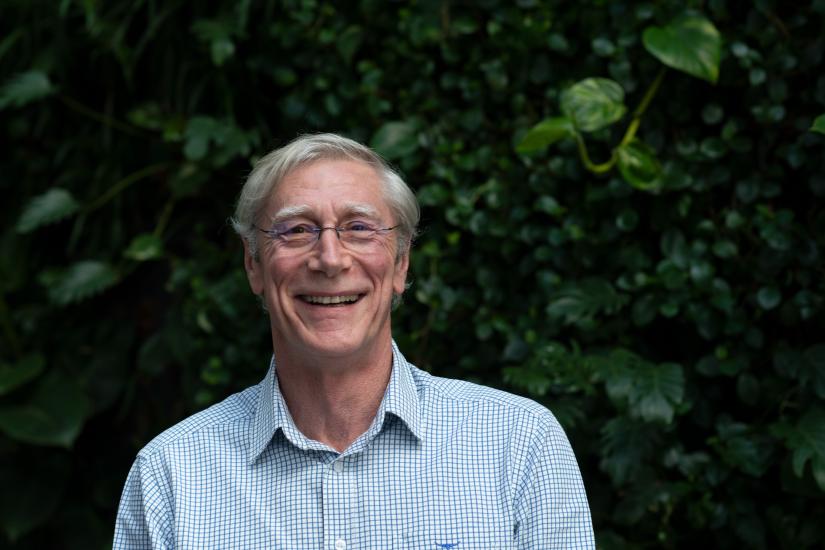 A man smiles at the camera, green plants in the background