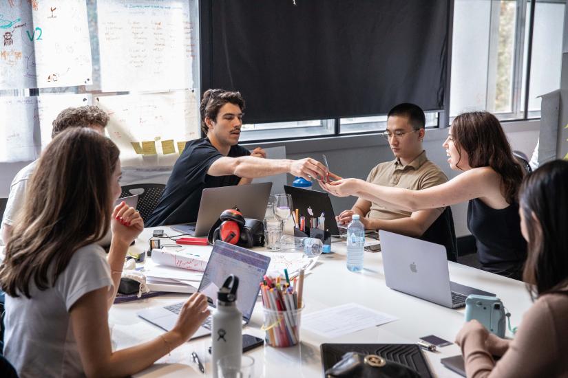 Students sitting at a table, passing post-it notes