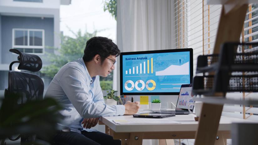 Person sitting at desk looking at multiple computer monitors with data analytics graphics on the screen
